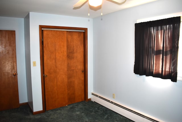 unfurnished bedroom featuring dark colored carpet, a closet, baseboard heating, and ceiling fan