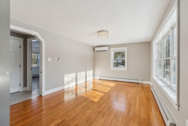 spare room with a wall mounted air conditioner, light hardwood / wood-style floors, and baseboard heating