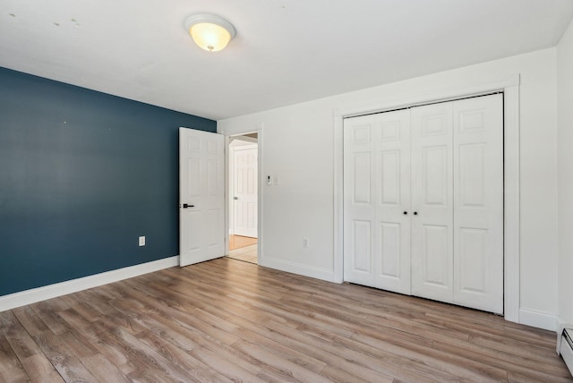 unfurnished bedroom with a baseboard radiator, light hardwood / wood-style floors, and a closet