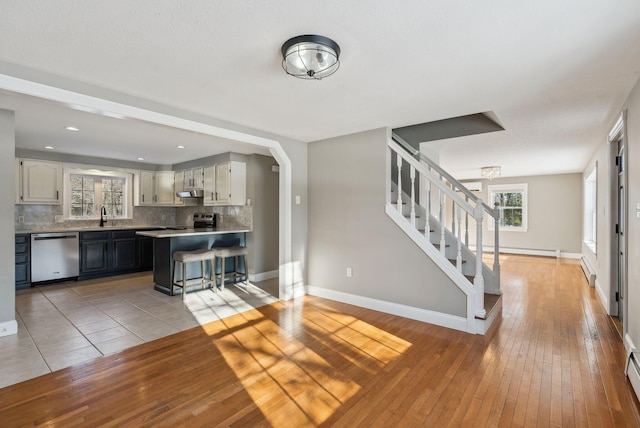 unfurnished living room with a baseboard radiator, sink, and light hardwood / wood-style flooring