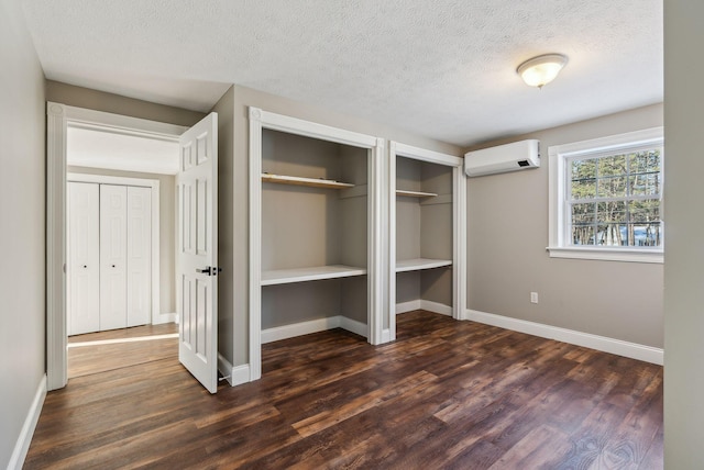 unfurnished bedroom featuring two closets, a wall mounted air conditioner, a textured ceiling, and dark hardwood / wood-style flooring