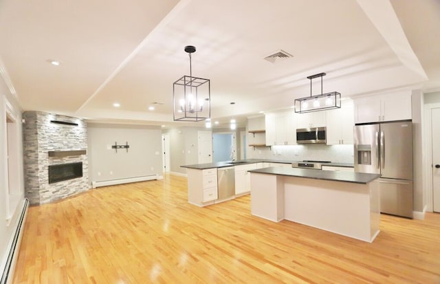 kitchen featuring baseboard heating, stainless steel appliances, a tray ceiling, white cabinets, and decorative light fixtures