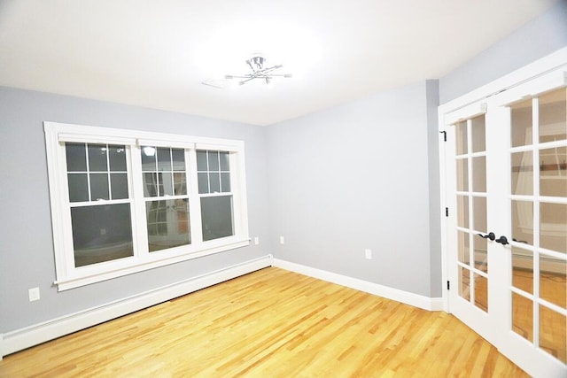 empty room with french doors, a baseboard heating unit, a chandelier, and hardwood / wood-style flooring