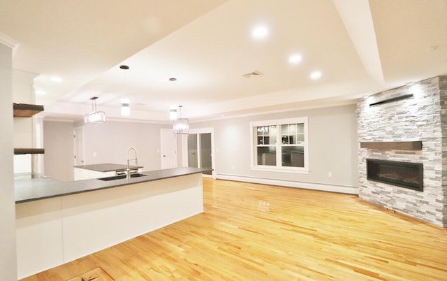 kitchen with a stone fireplace, decorative light fixtures, a baseboard heating unit, light wood-type flooring, and sink