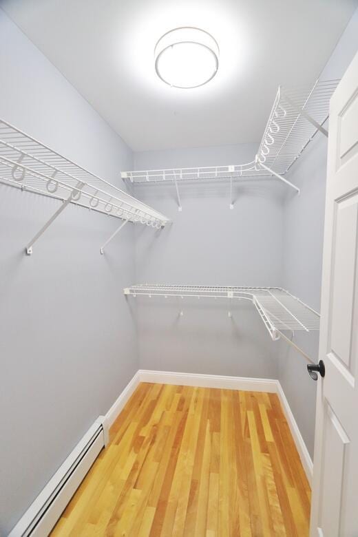 spacious closet with a baseboard heating unit and hardwood / wood-style flooring