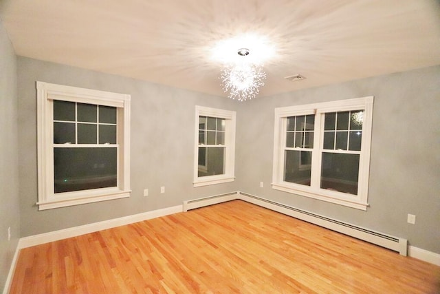 unfurnished room featuring a baseboard heating unit, hardwood / wood-style floors, and a notable chandelier