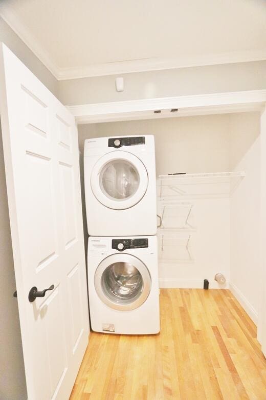 laundry area featuring stacked washer / drying machine, crown molding, and wood-type flooring