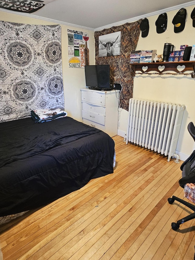 bedroom with wood-type flooring, radiator heating unit, and crown molding