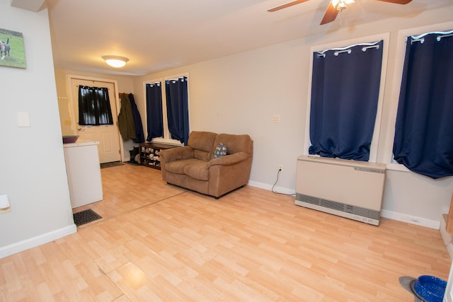 living room with heating unit, ceiling fan, and light wood-type flooring