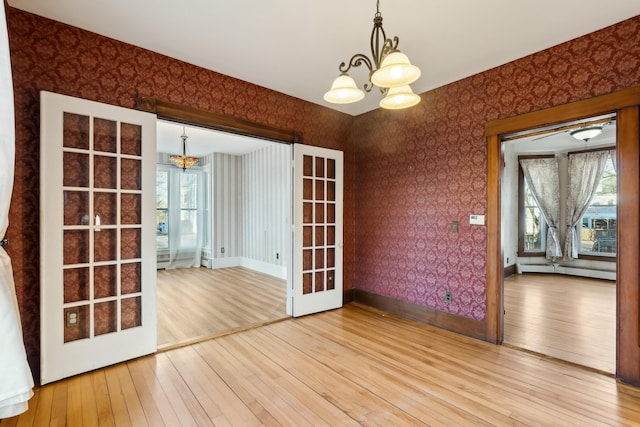 unfurnished dining area with french doors, an inviting chandelier, baseboard heating, and hardwood / wood-style floors