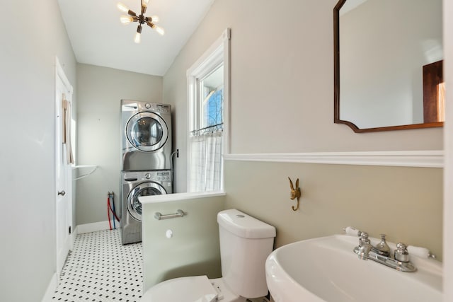 bathroom featuring a chandelier, stacked washer and dryer, toilet, and sink