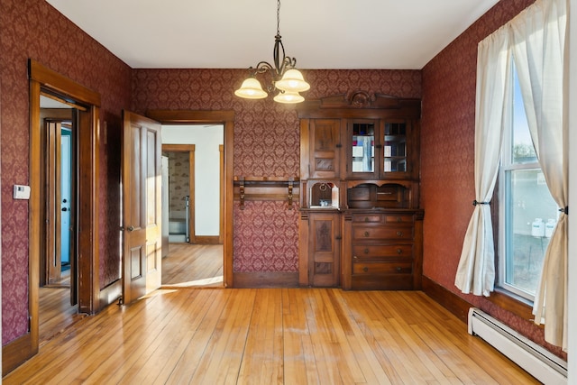 dining area with plenty of natural light, light hardwood / wood-style floors, baseboard heating, and an inviting chandelier