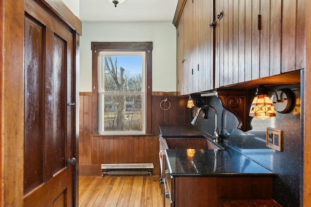 kitchen with light wood-type flooring, a baseboard heating unit, sink, dark stone countertops, and wood walls