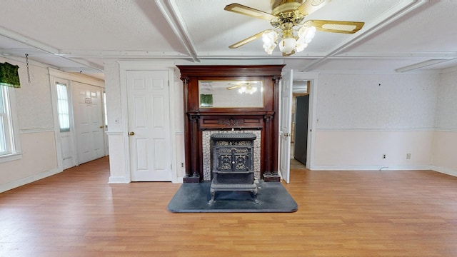 unfurnished living room with light wood-type flooring, ceiling fan, a textured ceiling, and a wood stove