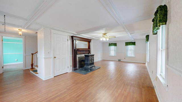 unfurnished living room featuring coffered ceiling, light hardwood / wood-style floors, ceiling fan, a wood stove, and beam ceiling