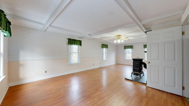 unfurnished living room with coffered ceiling, beamed ceiling, ceiling fan, a wood stove, and light hardwood / wood-style flooring