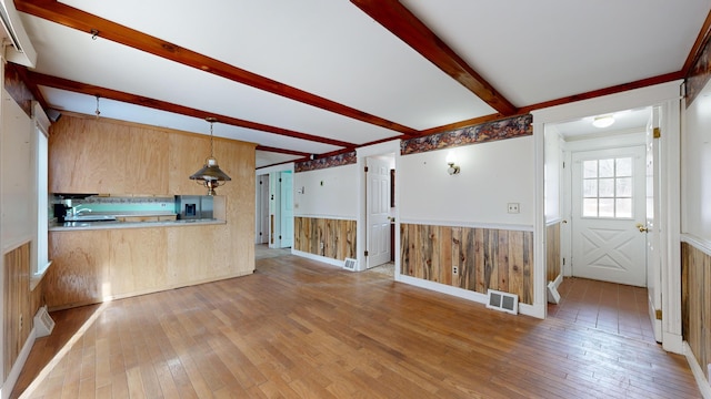 unfurnished living room featuring sink, beam ceiling, light hardwood / wood-style floors, and wooden walls