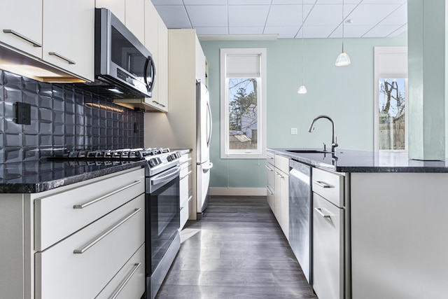 kitchen featuring tasteful backsplash, appliances with stainless steel finishes, white cabinets, decorative light fixtures, and sink