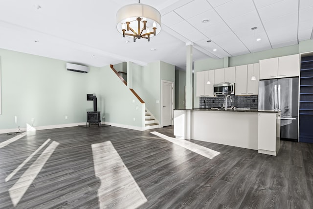 kitchen with appliances with stainless steel finishes, dark hardwood / wood-style flooring, a wall mounted air conditioner, a wood stove, and white cabinetry