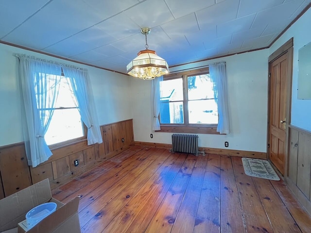 interior space with ornamental molding, hardwood / wood-style flooring, radiator heating unit, wood walls, and a notable chandelier