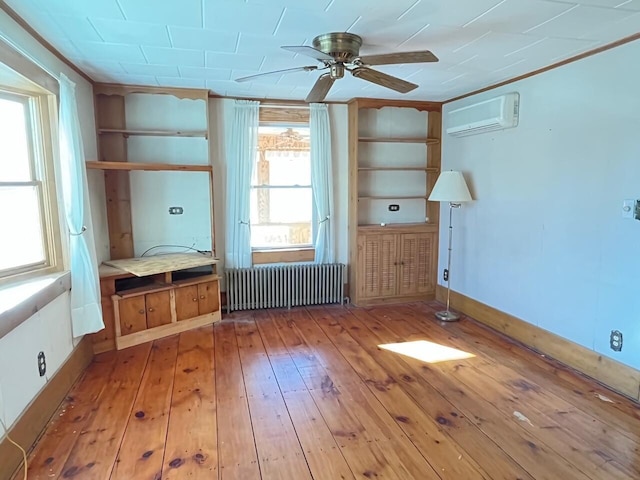 unfurnished room with ceiling fan, light hardwood / wood-style flooring, radiator, a wall mounted AC, and built in shelves