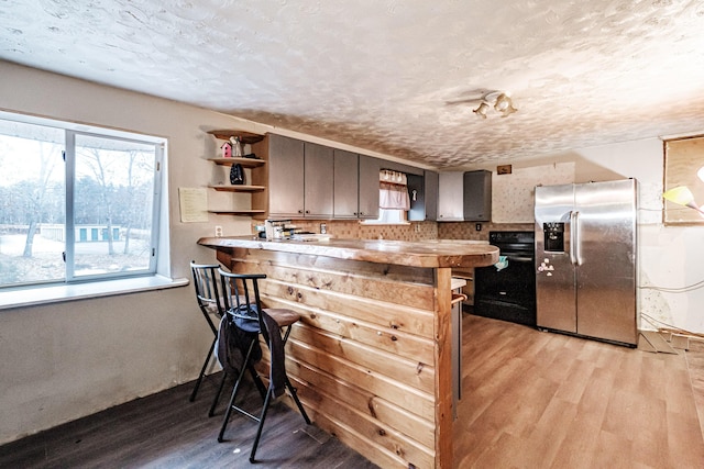 kitchen featuring a wealth of natural light, stainless steel fridge with ice dispenser, kitchen peninsula, light hardwood / wood-style floors, and a textured ceiling