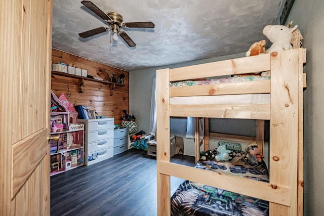 bedroom featuring ceiling fan, dark hardwood / wood-style floors, a textured ceiling, and wooden walls