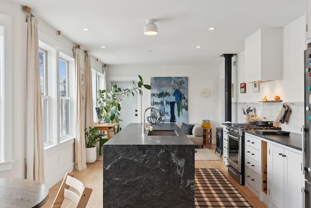 kitchen with light hardwood / wood-style flooring, high end range, a kitchen island with sink, white cabinets, and sink