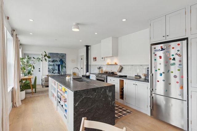 kitchen with sink, white cabinets, light hardwood / wood-style floors, a kitchen island with sink, and appliances with stainless steel finishes