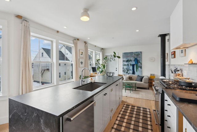 kitchen with a wood stove, a kitchen island with sink, white cabinetry, appliances with stainless steel finishes, and sink