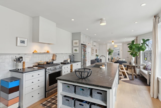 kitchen with sink, white cabinets, a kitchen island with sink, and stainless steel stove