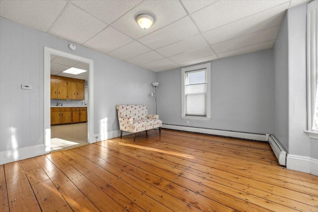 unfurnished room featuring a baseboard heating unit, sink, a drop ceiling, and light wood-type flooring