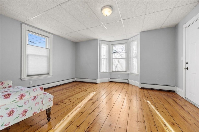 interior space featuring a drop ceiling, hardwood / wood-style flooring, and a baseboard heating unit