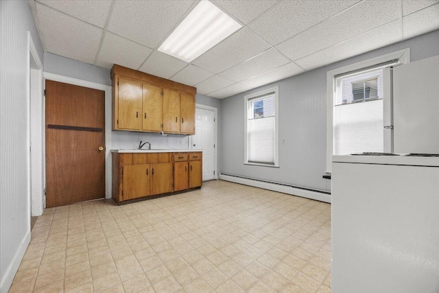 kitchen featuring sink, a drop ceiling, white fridge, and a baseboard heating unit