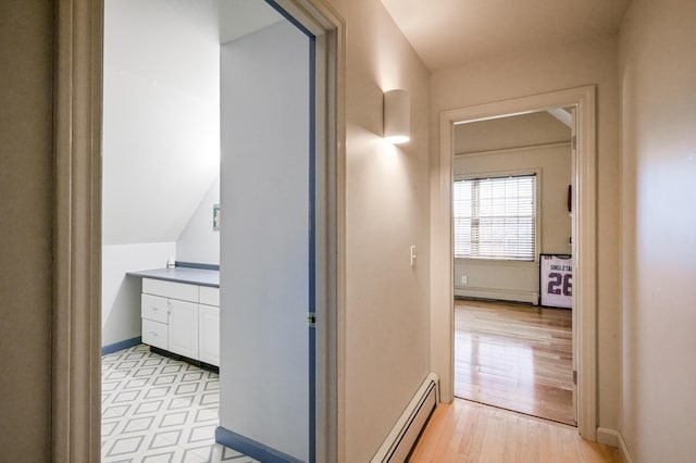 corridor with light hardwood / wood-style floors, lofted ceiling, and a baseboard heating unit