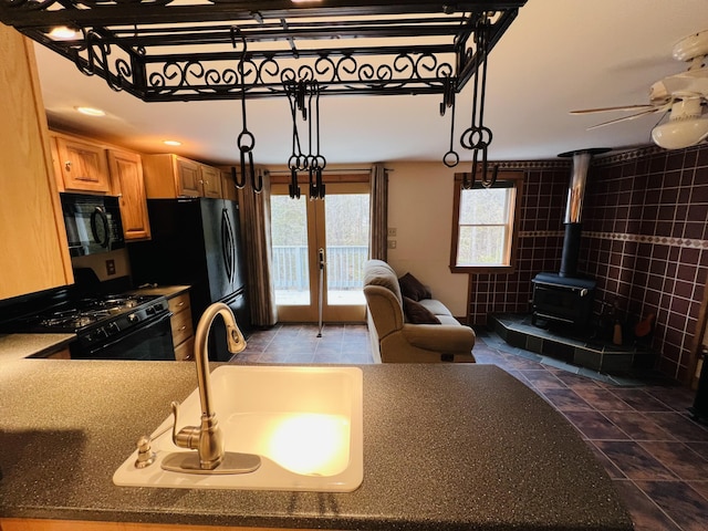 kitchen with ceiling fan, black appliances, sink, a wood stove, and french doors