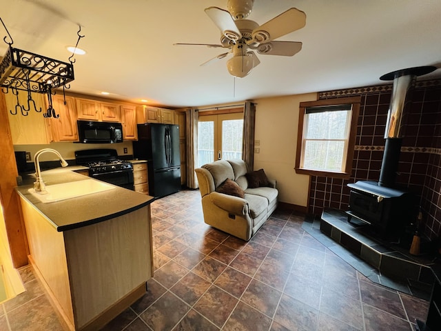 kitchen with ceiling fan, a wood stove, french doors, black appliances, and sink