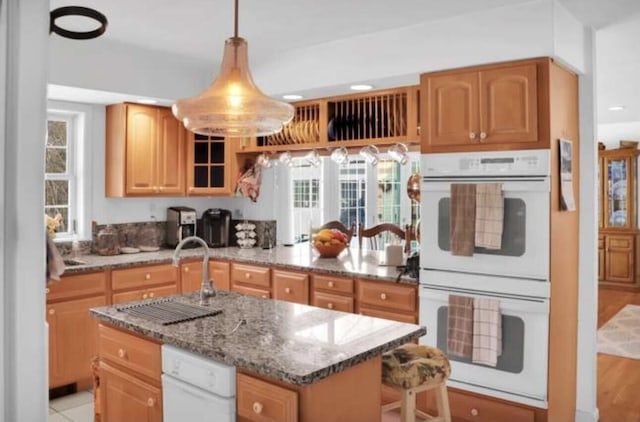 kitchen featuring sink, hanging light fixtures, light stone countertops, a kitchen island, and double oven