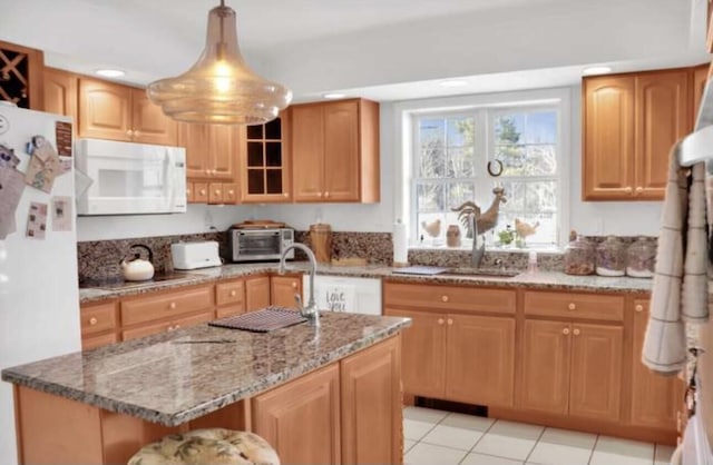 kitchen with white appliances, hanging light fixtures, a center island with sink, stone counters, and sink