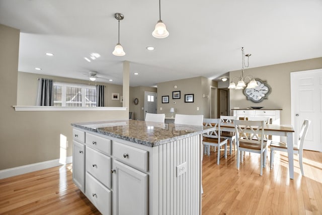 kitchen with a center island, light hardwood / wood-style floors, ceiling fan with notable chandelier, dark stone counters, and pendant lighting