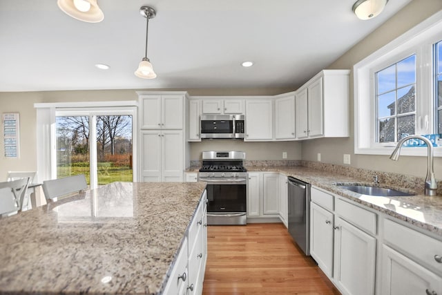 kitchen featuring stainless steel appliances, sink, decorative light fixtures, white cabinets, and light stone countertops