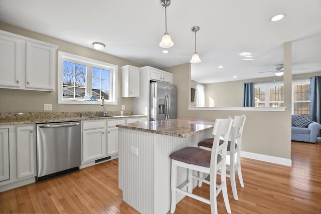 kitchen featuring appliances with stainless steel finishes, a center island, pendant lighting, white cabinets, and sink