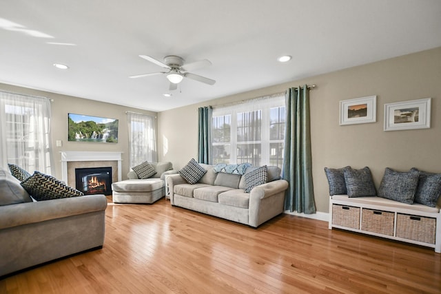 living room with a tile fireplace, ceiling fan, and light hardwood / wood-style flooring