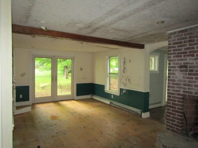 unfurnished room featuring baseboard heating, a wealth of natural light, beamed ceiling, and a brick fireplace