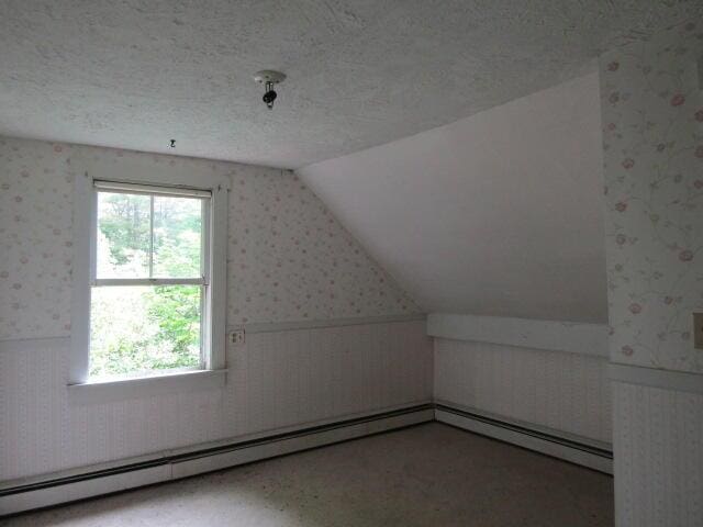 bonus room with vaulted ceiling, a textured ceiling, and a baseboard heating unit