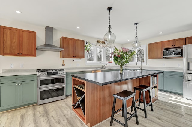 kitchen with wall chimney exhaust hood, stainless steel appliances, light hardwood / wood-style floors, a kitchen island, and sink