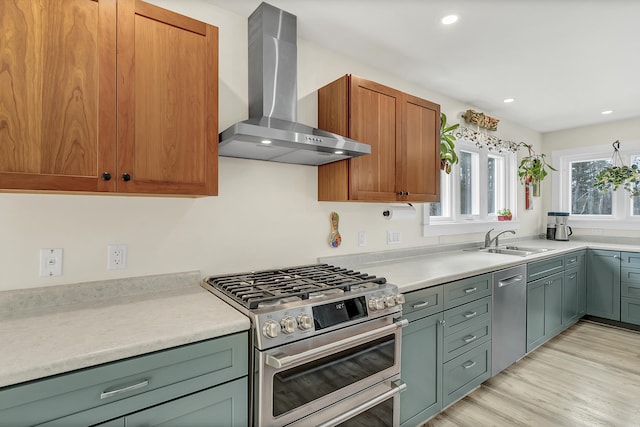 kitchen with sink, wall chimney range hood, light hardwood / wood-style flooring, and appliances with stainless steel finishes