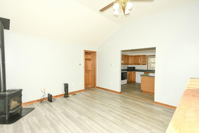 unfurnished living room featuring ceiling fan, light wood-type flooring, a wood stove, and vaulted ceiling