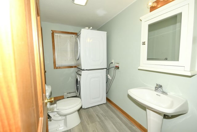 bathroom featuring sink, toilet, baseboard heating, wood-type flooring, and stacked washer / dryer