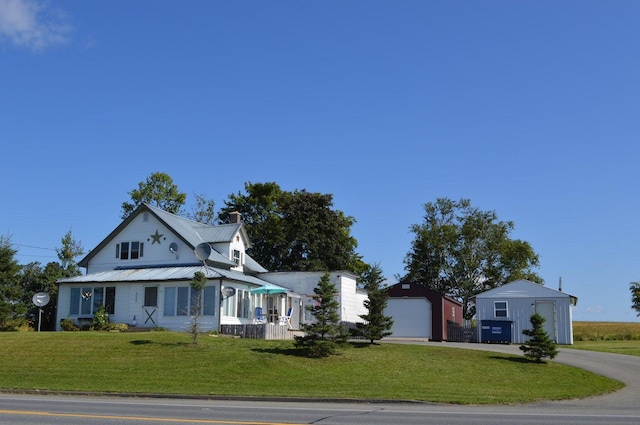 view of front facade featuring metal roof, a garage, an outdoor structure, driveway, and a front lawn